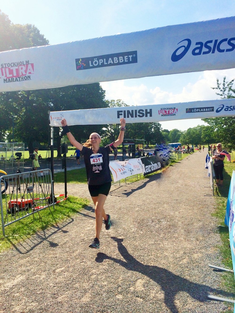 Sexual assault survivor Laurel. She crosses the finish line at a race, holding her hands above her head as she runs. 