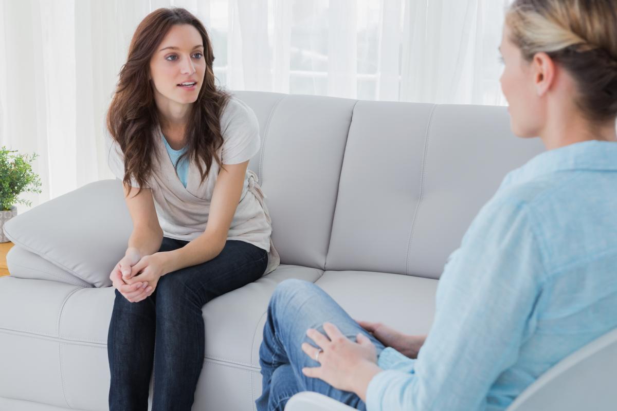 One woman is seated on another couch addressing another woman who is her therapist